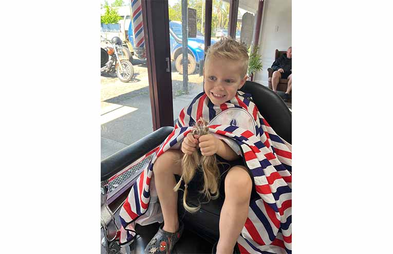 A new-look Tommy holding his shorn locks. Photo: Supplied.